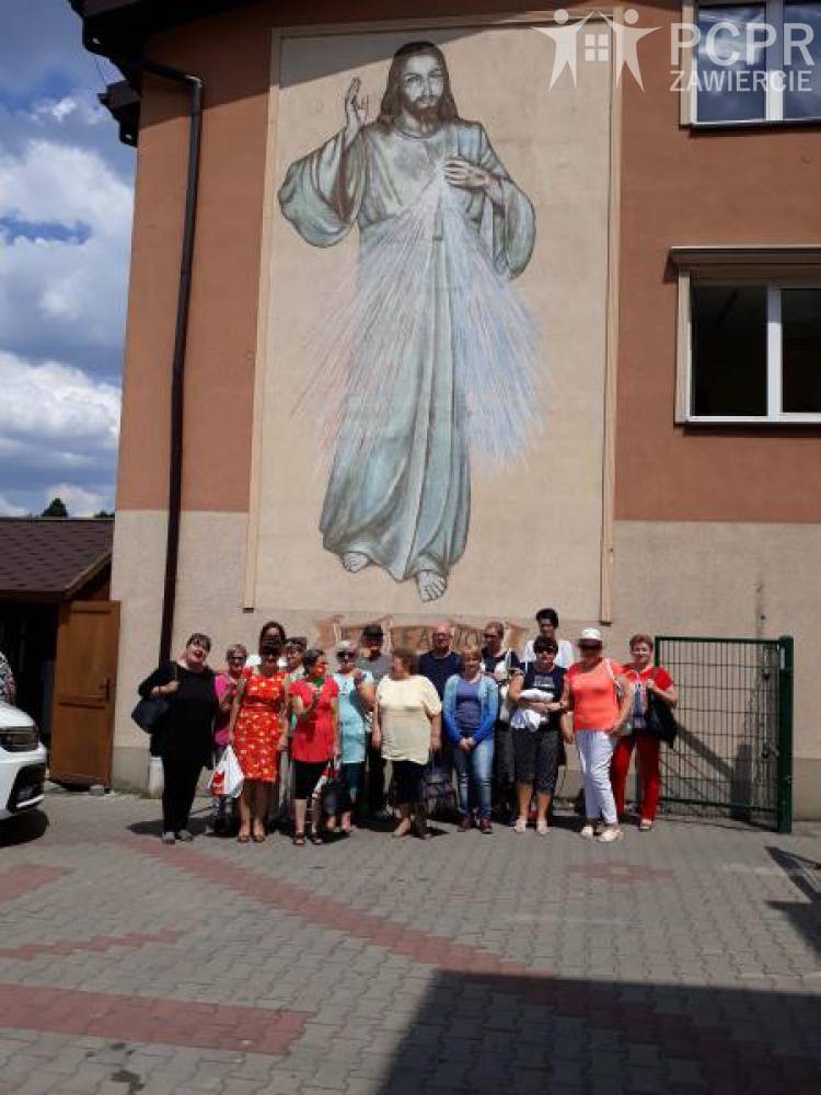 Zdjęcie: Grupa kobiet i mężczyzn stoi na tle budynku na którym znajduje się wizerunek Jezusa